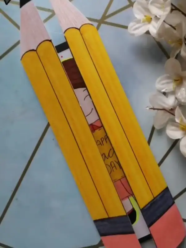 15 Easy Paper Crafts DIY for Teachers: Quick Classroom Wins 8 Two tall yellow paper pencils parting to reveal a hand drawn figure holding a Happy Teacher's Day sign.