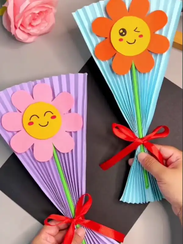 15 Easy Paper Crafts DIY for Teachers: Quick Classroom Wins 6 Two pleated paper flower bouquets in purple and blue, with smiling flower faces and red ribbon bows.